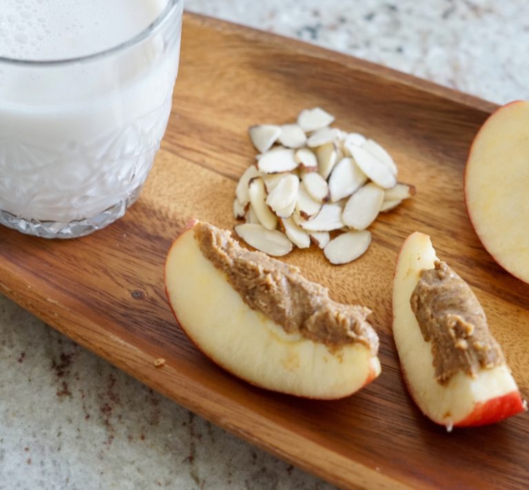 Slivered almonds, almond butter on apple slices and almond milk on a wooden tray