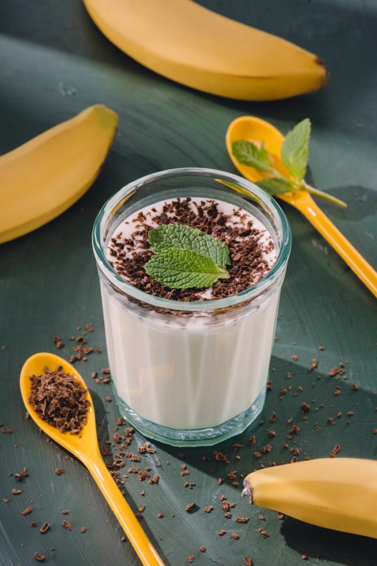 closeup shot of milkshake with mint leaves and chocolate shavings, spoons and bananas